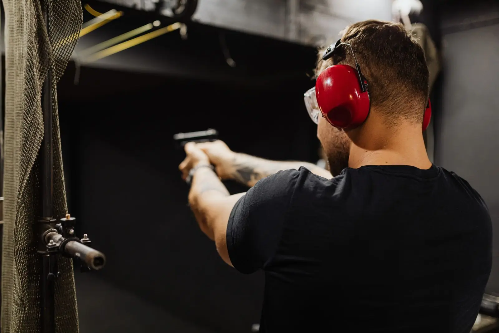 Man with ear protection firing a handgun at an indoor range